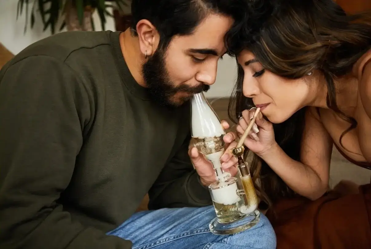 Two people at a sesh using a joint to smoke a bowl in typical stoner things fashion.
