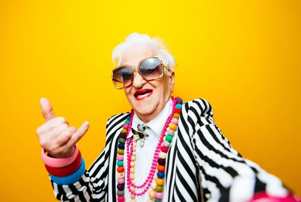 A funky weed-loving grandma dressed eccentrically flashes a shaka sign while living the stoner lifestyle.