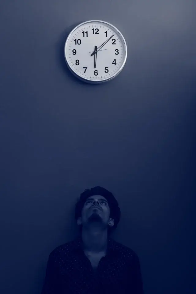 A man with insomnia stares sadly up at a clock and considers using cannabis to improve his sleep and productivity.